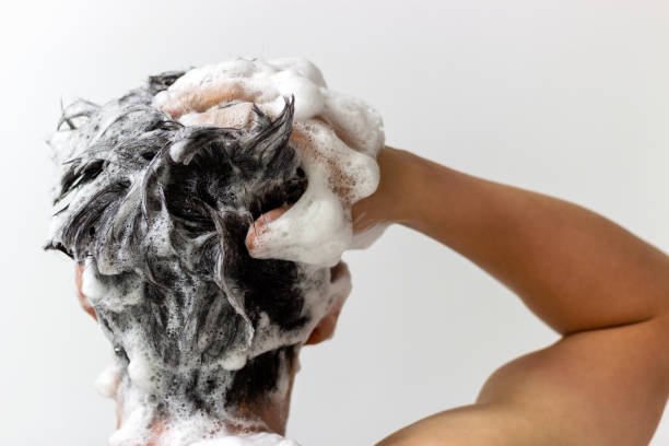 A man washes his head with shampoo on a white background, rear view